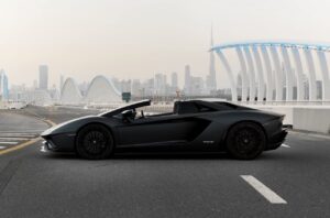 Matte black Lamborghini Aventador Ultimae parked on Dubai bridge with skyline view.