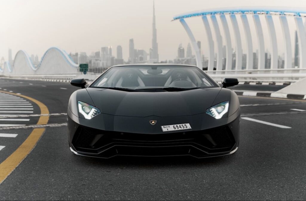 Matte black Lamborghini Aventador Ultimae parked on Dubai bridge with skyline view.