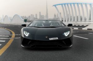 Matte black Lamborghini Aventador Ultimae parked on Dubai bridge with skyline view.