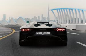 Matte black Lamborghini Aventador Ultimae parked on Dubai bridge with skyline view.